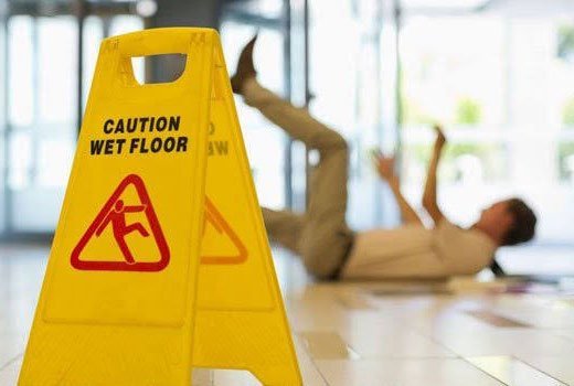 A wet floor caution sign with a person slipping in the background