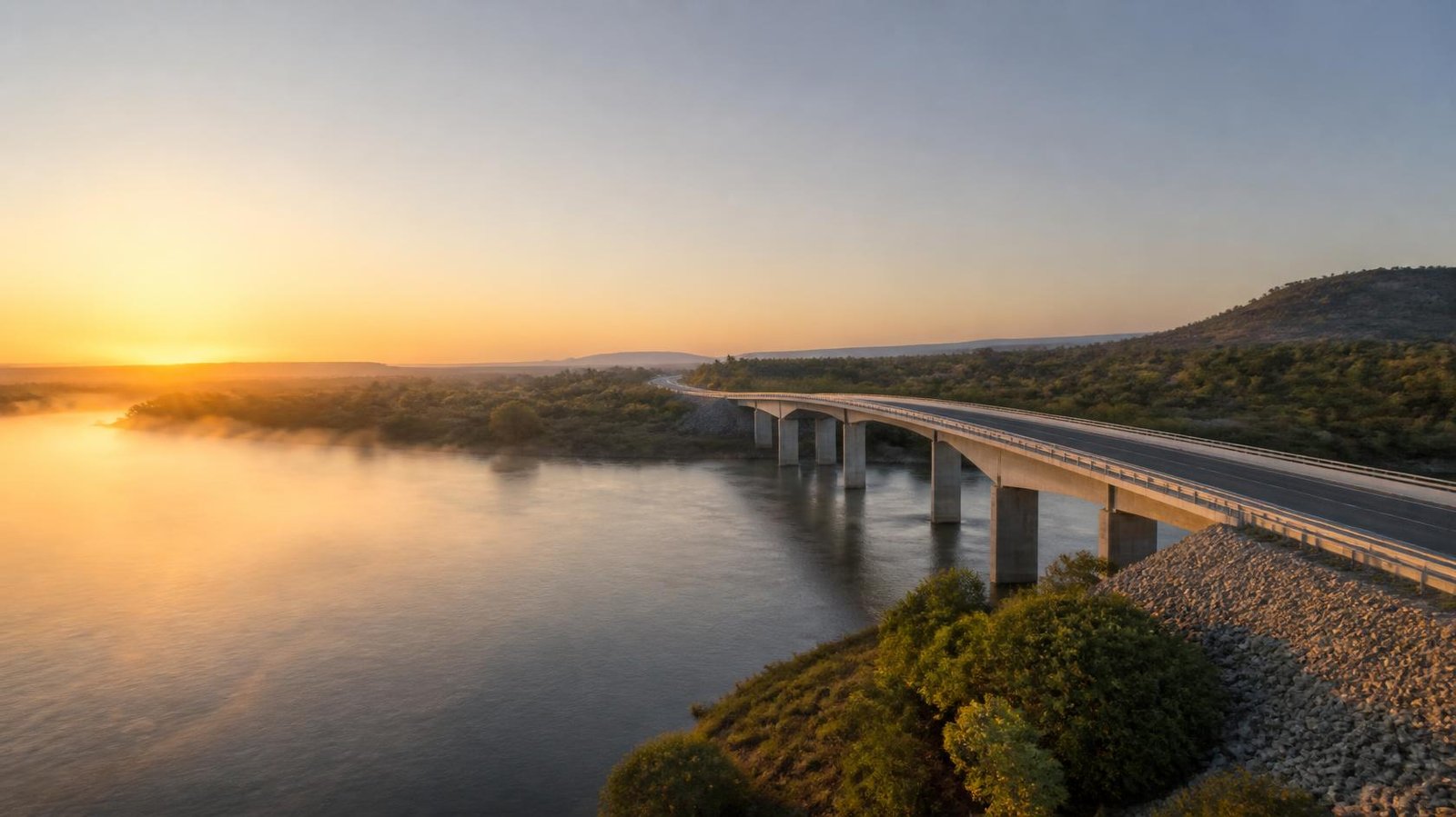 A completed road bridge crossing a river at sunrise